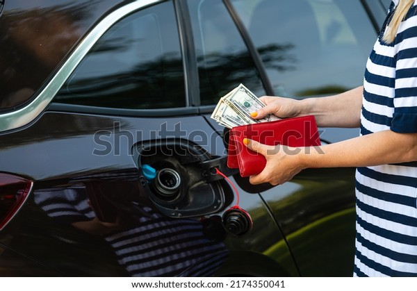 a woman s hand counts money\
while standing at an open fuel tank, the concept of rising fuel\
prices