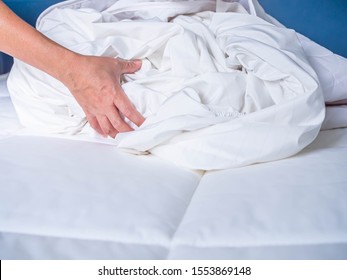 Woman 's hand with crumpled and wrinkle white bed cover on the bed in the bedroom. Housework preparation before laundry process.