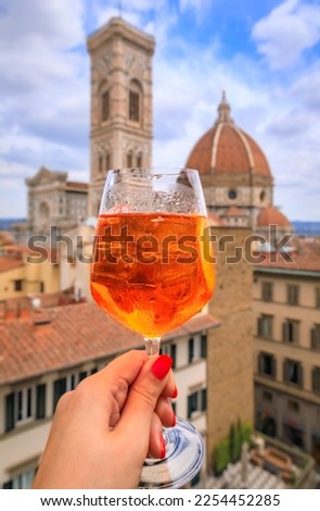 Woman s hand holding an orange Spritz cocktail with a view of the Duomo Cathedral or Cattedrale di Santa Maria del Fiore in Florence, Italy