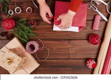 Woman s hands wrapping Christmas gift, close up. Unprepared christmas presents on wooden background with decor elements and items, top view. Christmas or New year DIY packing Concept. - Powered by Shutterstock