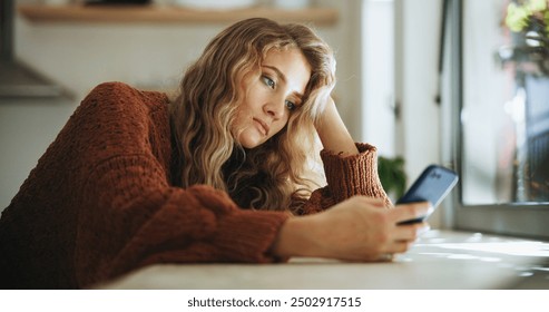 Woman, sad and smartphone in home for reading, chat and message of break up with online partner. House, girl and mobile app with social media for beauty standards, cyberbullying and trolling comment - Powered by Shutterstock