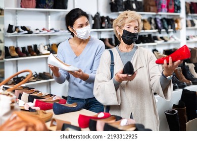 Woman Sales Consultant In A Protective Mask, Working In A Shoe Store During The Pandemic, Helps A Mature European Woman ..buyer Choose Ballet Flats