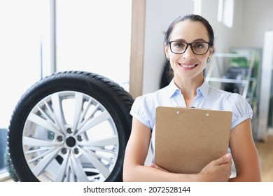 Woman Salesman With Glasses Holding Clipboard With Documents In Auto Repair Shop Portrait. Tire Fitting Services Concept