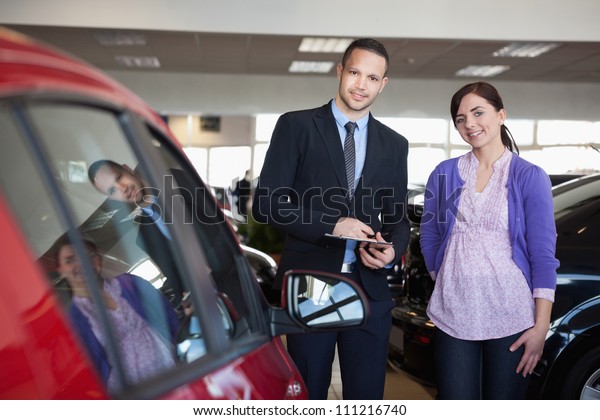 Woman\
and a salesman standing side by side in a car\
shop