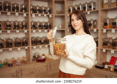 woman salesman at tea shop smiles, offers goods. Natural Chinese tea in glass jars. portrait - Powered by Shutterstock