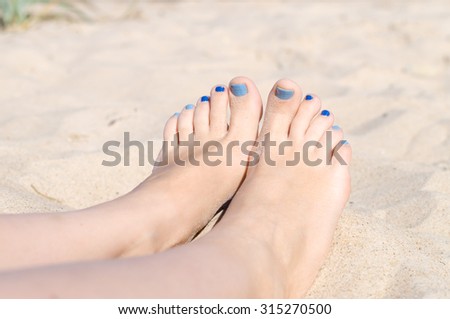 Woman sandy feet with blue nails pedicure relaxing on the beach
