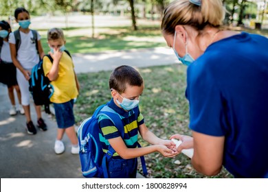 Woman Sanitizing School Children's Hands Outdoors