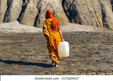 woman in a sari and hijab carries a plastic jerrican with water over a lifeless desert valley