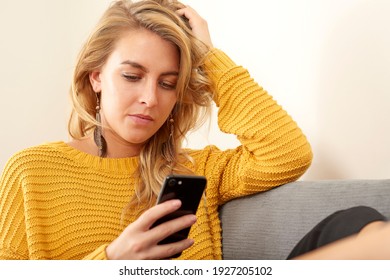 Woman Sat On Sofa Texting On Mobile Phone