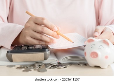 Woman Save Money In Piggy Bank And Calculating Book Bank Statement For Household Expense. Home Accounting Plan For Monthly Payment Using Calculator And Piggy Bank. Saving Concept At Home.