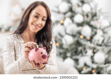 Woman saving money for Christmas while putting a two euro coin into a piggy bank.