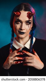 woman with scary halloween makeup with bloody horns on dark background looking forward with yellow eyes hands with blood