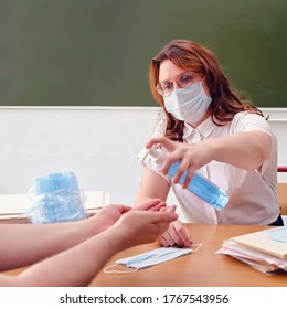 Woman schoolteacher treats hands with antiseptic. Female doctor in medical mask uses hand sanitizer sitting at a desk, copy space. Classroom safety concept during lessons in the coronavirus epidemic - Powered by Shutterstock