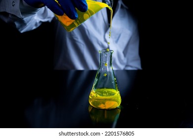 A Woman Scientist Experimenting With A Yellow Fluorescent Solution In A Glass Conical Flask In Dark Biomedical Laboratory For Health Care Medicine Development. Copy Space Black Background