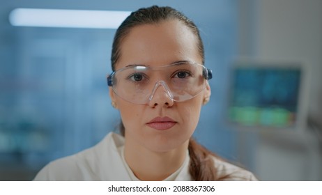 Woman Scientist With Protective Glasses In Laboratory, Looking At Camera. Portrait Of Biochemistry Researcher Wearing Lab Goggles For Safety At Chemical Development Work. Close Up