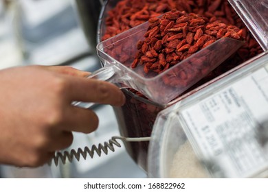 Woman Scooping Goji Berries From The Bulk Food Dispenser At An Organic Grocery Store