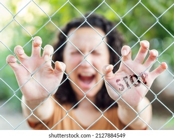 Woman screaming behind a fence with the word stop written on her hand. Concept of feminism, demand for equality and an end to violence against women. Concept of stop war. Selective focus.