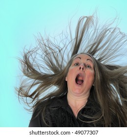 A woman screaming in front of a blue background with her hair blasting behind her.
