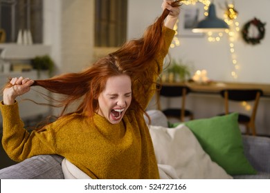 woman screaming and pulling at her long red hair with christmas decoration in background