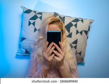 Woman Scrolling Through Her Phone While Laying In Bed. Sleepless, Late Night Internet Browsing