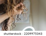 Woman scrunching her hair to form curls. Applying curly method for hair styling