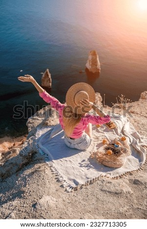 woman sea trevel. photo of a beautiful woman with long blond hair in a pink shirt and denim shorts and a hat having a picnic on a hill overlooking the sea