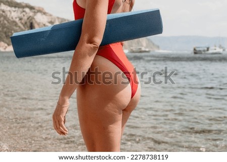 Woman sea yoga. Happy women in red bikini and yoga mat on the beach, ocean and rock mountains. Motivation and inspirational fit and exercising. Healthy lifestyle outdoors in nature, fitness concept.