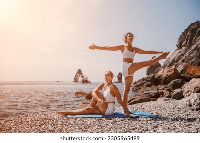 Woman sea yoga. Two happy women practicing yoga on the beach with ocean and rock mountains. Motivation and inspirational fit and exercising. Healthy lifestyle outdoors in nature, fitness concept. - Powered by Shutterstock