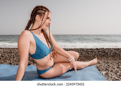 Woman sea yoga. Well looking middle aged woman with braids dreadlocks in blue swimwear doing stretching pilates on yoga mat near sea. Female fitness yoga routine concept. Healthy lifestyle.
