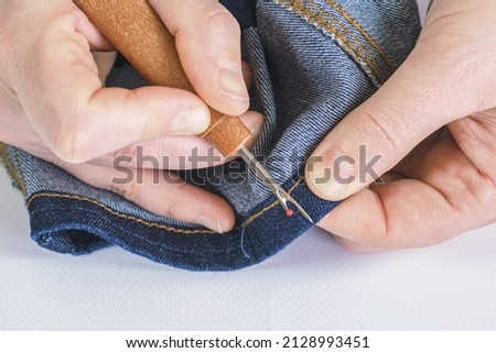 Woman seamstress rips a seam on a denim fabric with a seam ripper. Seamstress tools, mending clothes, altering jeans.