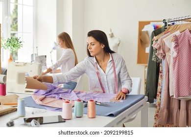 Woman seamstress sit at table design garment in fashion atelier with colleague. Female designer or tailor create clothing piece in workshop, work with fabric textile. Style, dressmaking concept.