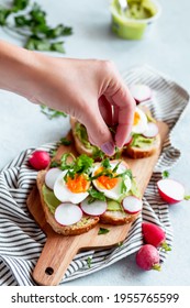 Woman Seasoning Avocado And Egg Toasts For Breakfast With Herbs, Top View