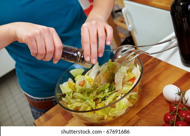 Woman seasoning salad with black pepper from a mill