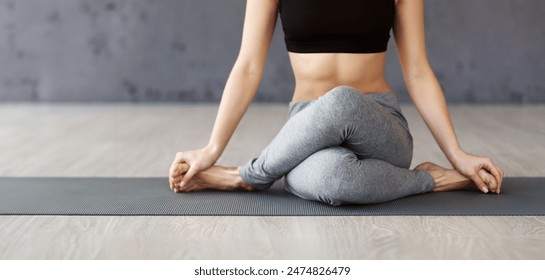 A woman is seated in a cross-legged position on a yoga mat, performing a yoga pose in a bright studio during the morning. - Powered by Shutterstock