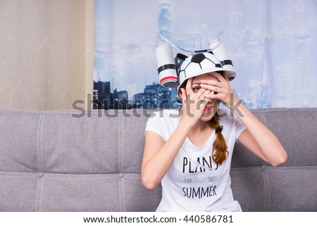 Woman seated on couch covers her face and peeks out as image of city skyline hangs on canvas behind her