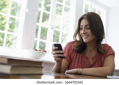 A woman seated at a table, checking her smart phone.