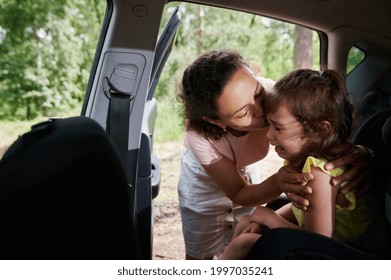 Woman Seats The Child In The Child's Car Seat. Mom Consoles Her Crying Baby Girl, Who Doesn't Want To Sit In A Car Seat.