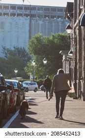 Woman Seen From Behind Walking Her Dog In Old Montreal, Facing The Sun