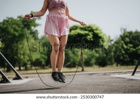 A woman is seen exercising with a jump rope outdoors in a park, enjoying a summer day while staying fit and active.