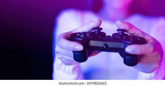 A woman is seen holding a video game controller in front of a vibrant purple light, engaged in a gaming session. The controller is illuminated by the vivid purple glow, creating a striking contrast. - Powered by Shutterstock