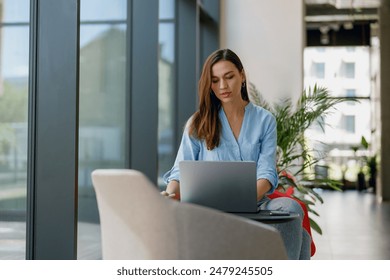 A woman is seen inside a contemporary green office, concentrating on work using a laptop - Powered by Shutterstock