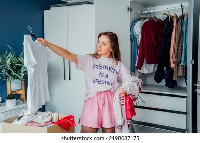Woman selecting clothes from her wardrobe for donating to a Charity shop. Decluttering, Sorting clothes and Cleaning Up. Reuse, second-hand concept. Conscious consumer, sustainable lifestyle. - Shutterstock ID 2198087175