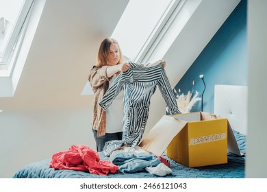 Woman selecting clothes from her wardrobe for recycling, donating to a Charity shop. Decluttering, Sorting clothes, Cleaning Up. Reuse, second hand concept. Conscious consumer, sustainable lifestyle. - Powered by Shutterstock