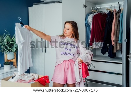 Woman selecting clothes from her wardrobe for donating to a Charity shop. Decluttering, Sorting clothes and Cleaning Up. Reuse, second-hand concept. Conscious consumer, sustainable lifestyle.