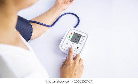 Woman Self-checks Her Blood Pressure And Heart Rate Monitor With A Digital Pressure Monitor At Home. Health Care And Medical Concepts