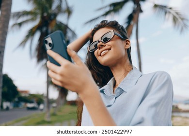 Woman selfie, sunglasses, palm trees, street sign a woman wearing sunglasses takes a selfie with her cell phone in front of a palm tree and a street sign, with additional palm trees in the background - Powered by Shutterstock