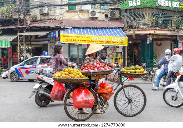 Woman is selling fruits from bicycle on\
the street in Hanoi, Vietnam - December 23, 2018 Street vendor in\
Hanoi, Vietnam is selling fruits from his\
bicycle.