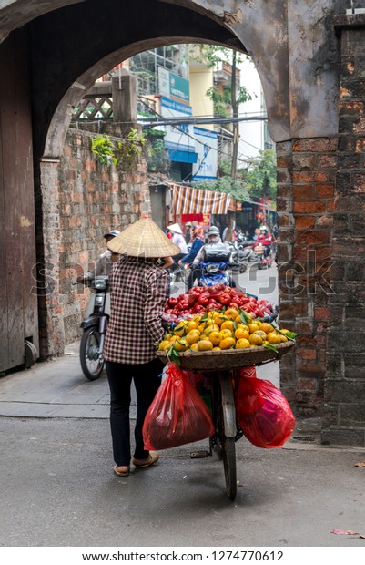 Woman is selling fruits from bicycle on\
the street in Hanoi, Vietnam - December 23, 2018 Street vendor in\
Hanoi, Vietnam is selling fruits from his\
bicycle.