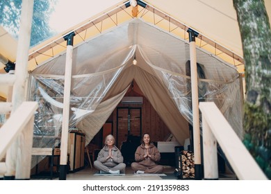 Woman Senior And Young Relaxing At Glamping Camping Tent. Women Family Elderly Grandmother And Young Granddaughter Doing Yoga And Meditation Indoor. Modern Zen-like Vacation Lifestyle Concept