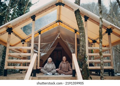 Woman Senior And Young Relaxing At Glamping Camping Tent. Women Family Elderly Mother And Young Daughter Doing Yoga And Meditation Indoor. Modern Zen-like Vacation Lifestyle Concept